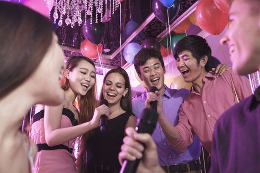 Group of friends holding microphones in a nightclub and singing together karaoke