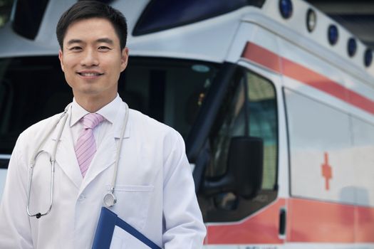 Portrait of smiling doctor holding clipboard in front of an ambulance