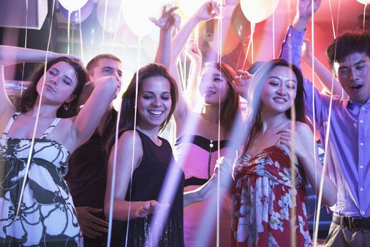 Multi-ethnic group of friends with hands in the air dancing among balloons in a nightclub
