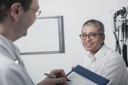 Doctor writing on medical chart with a smiling patient