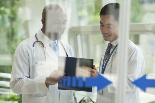 Two doctors consulting over medical record on the other side of glass doors