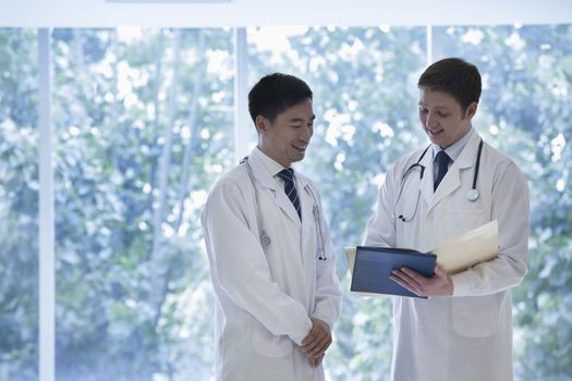 Two doctors standing, looking down, and consulting over medical record in the hospital