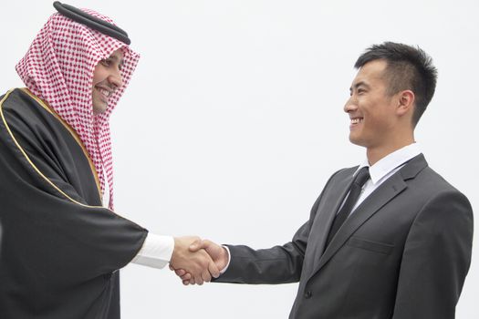 Smiling businessman and young man in traditional Arab clothing shaking hands, studio shot