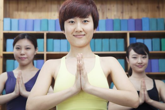 Three young women with hands clasped together in front doing yoga