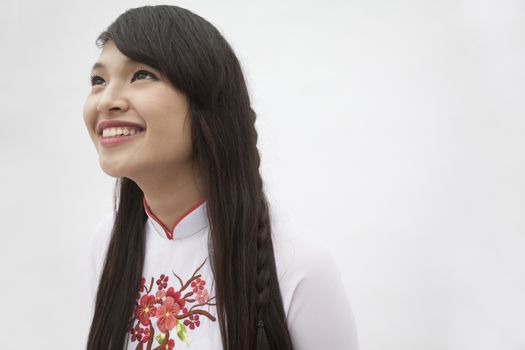 Portrait of smiling young woman with long hair wearing a traditional dress from Vietnam, studio shot
