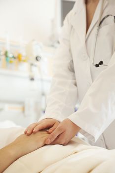 Close up of doctor holding a patients hands lying down on a hospital bed