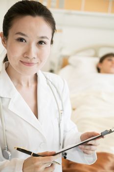 Portrait of smiling doctor holding a medical chart with patient lying in a hospital bed in the background