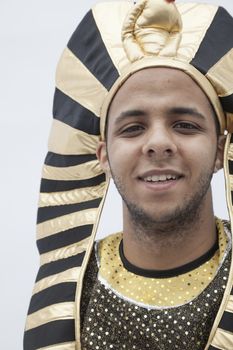 Portrait of smiling young man wearing a headdress from ancient Egypt, studio shot