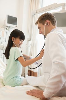 Girl patient checking the doctors heart beat with a stethoscope on a hospital bed