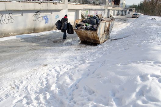 man carries four large black bags of garbage from the house to the container