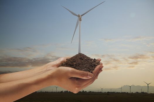 Hands holding soil with a wind turbine growing out from the middle