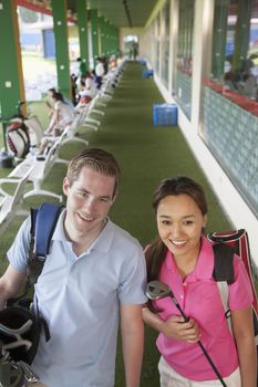 Young happy couple leaving the golf course with golf clubs and caddy