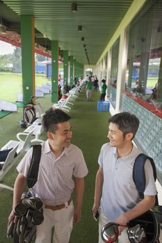 Two male friends smiling and getting ready to leave the golf course