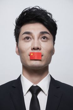Young businessman looking up with a Chinese flag covering his mouth