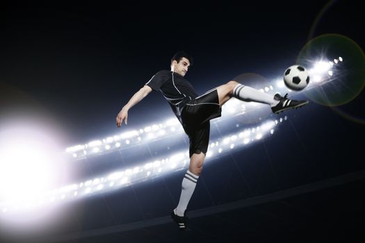 Soccer player in mid air kicking the soccer ball, stadium lights at night in background