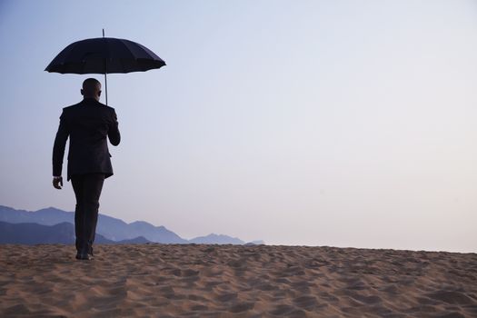 Businessman holding an umbrella and walking away in the middle of the desert