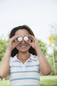 Smiling young woman holding up golf balls in front of her eyes