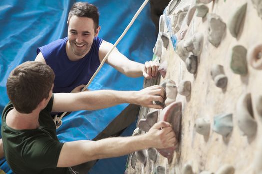 Two young men smiling at each other and climbing in an indoor climbing gym