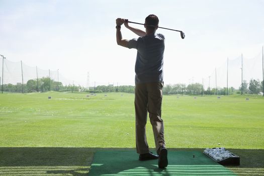 Rear view of young man hitting golf balls on the golf course, arms raised