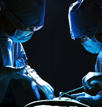 Two surgeons looking down, working, and holding surgical equipment with patient lying on the operating table 