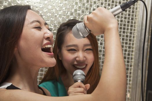 Two young female friends singing into a microphone at karaoke