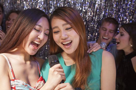 Group of friends singing into a microphone at karaoke