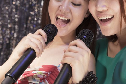 Close-up of two friends holding microphones and singing together at karaoke