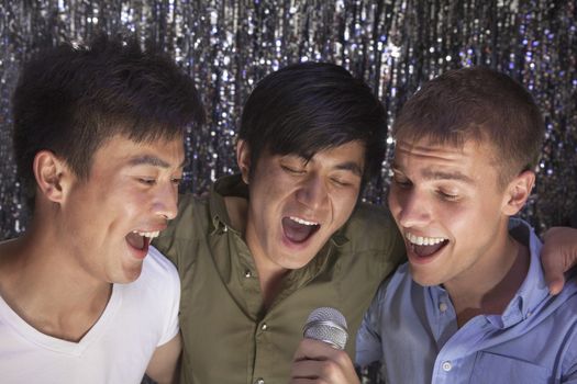 Three friends with arm around each other holding a microphone and singing together at karaoke