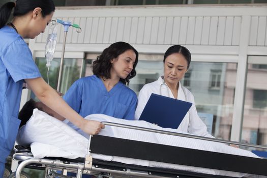 Paramedics and doctor looking down at the medical record of patient on a stretcher in front of the hospital