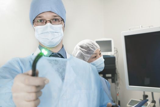 Portrait of young surgeon holding a medical instrument towards the camera, light shining