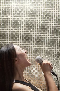 Side view of young woman singing into a microphone at karaoke, shiny background