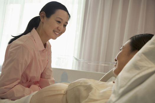 Smiling nurse talking to pregnant woman lying on bed in the hospital