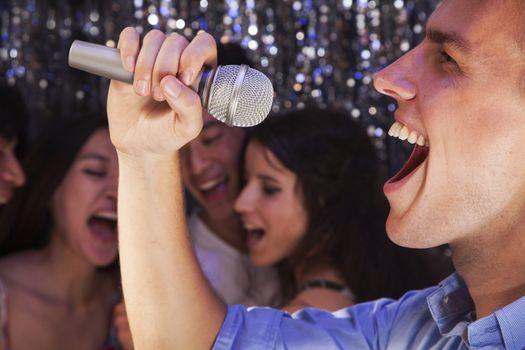Close- up of young man holding a microphone and singing at karaoke, friends singing in the background
