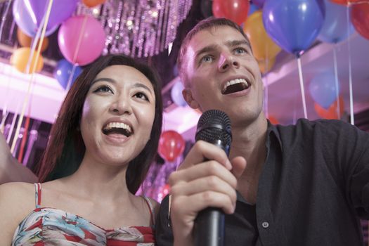 Two friends singing into a microphone together in a nightclub for karaoke