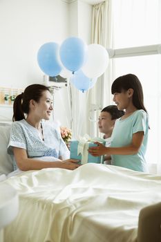 Girl and boy visiting their mother in the hospital, giving present and balloons
