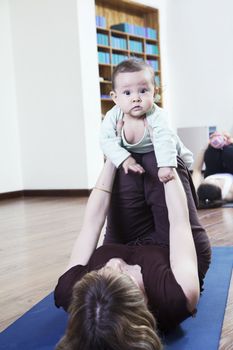 Mother lying on back and holding her baby during a yoga class