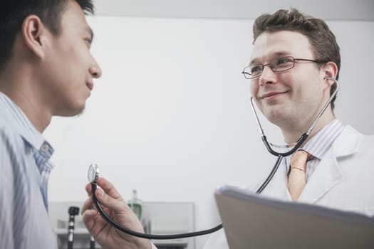 Smiling doctor checking heartbeat of a patient with a stethoscope
