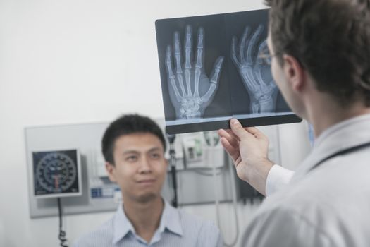 Doctor holding up and looking at x-ray of patients hand bones, patient in the background