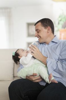 Father holding and feeding his baby daughter on the couch