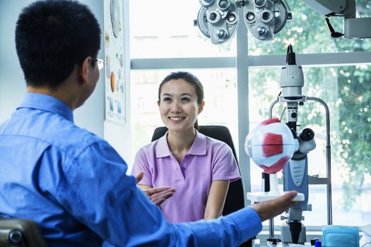 Optometrist discussing with young woman in his clinic