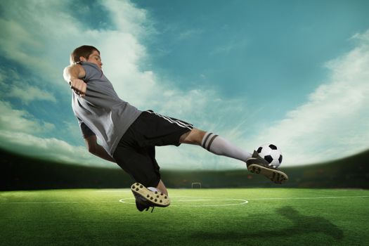 Soccer player kicking the soccer ball in mid air, in the stadium with the sky 