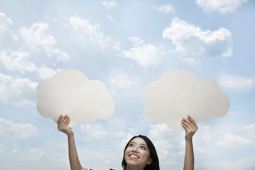 Young woman holding two cut out paper clouds against a blue sky with clouds