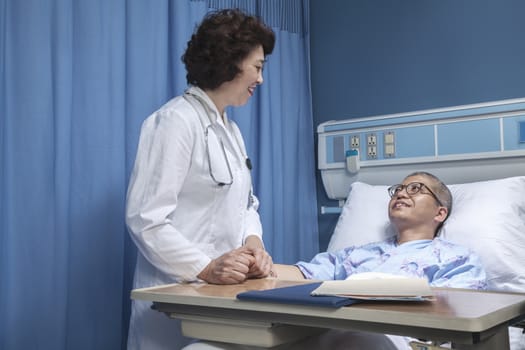 Smiling doctor checking up on a patient lying down in a hospital bed, holding hands