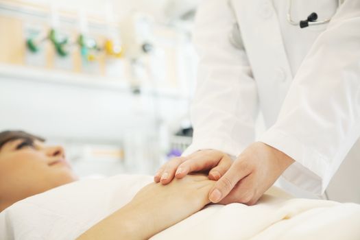 Close up of doctor holding a patients hands lying down on a hospital bed