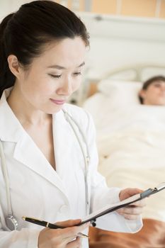 Portrait of smiling doctor holding a medical chart with patient lying in a hospital bed in the background