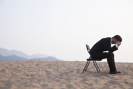 Businessman sitting with his head in his hands in the middle of the desert