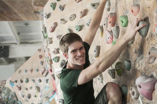 Smiling young man climbing up a climbing wall in an indoor climbing gym