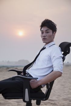 Businessman sitting on a chair and looking at camera in the middle of the desert