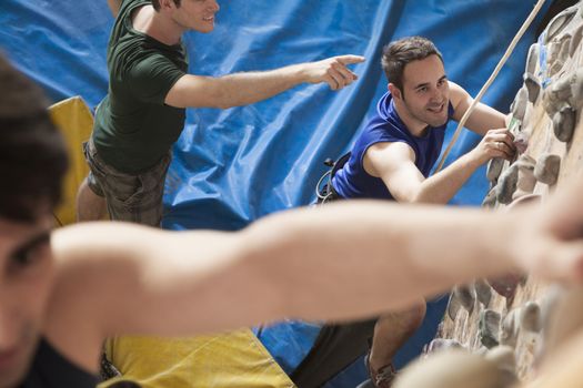 Three young men point and climbing in an indoor climbing gym