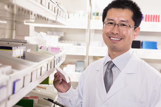 Pharmacist taking down and examining prescription medication in a pharmacy, looking at camera